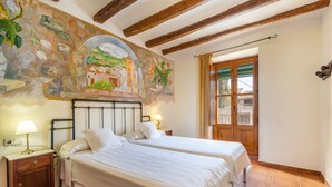 A room with two beds, a mural, wooden beams, a door with glass panels, and a nightstand with a lamp.