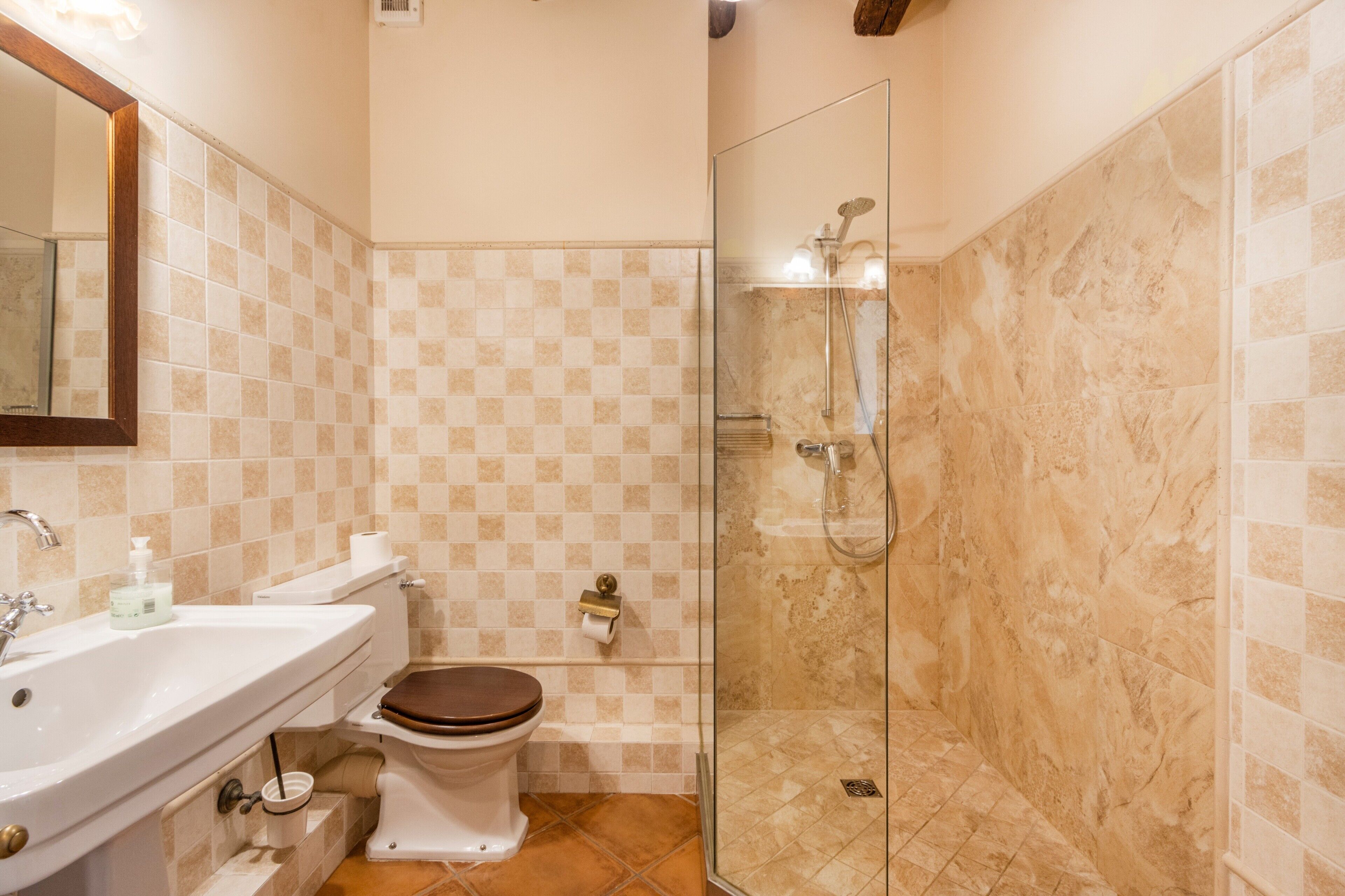 Et badeværelse med toilet, vask og glasvæg omkring brusebad.