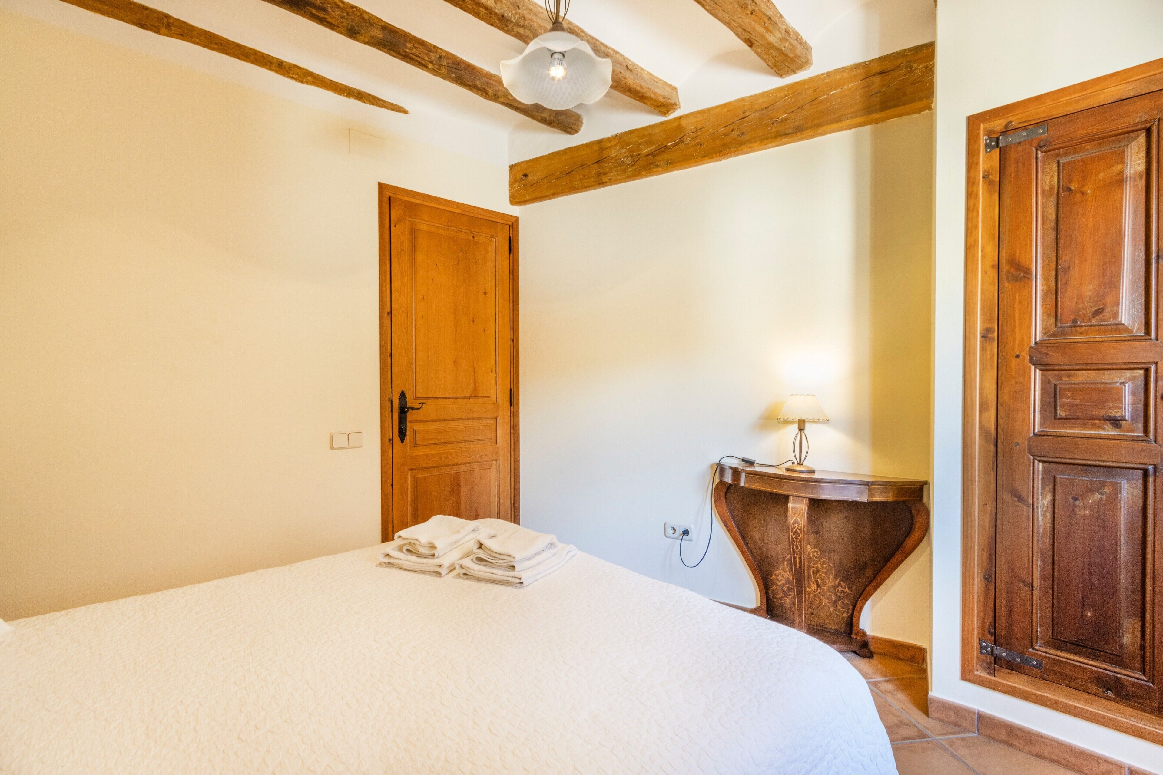 A bedroom with a bed, wooden door, and a bedside table with a lamp.