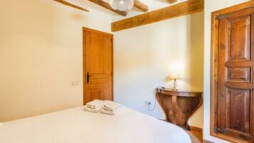A bedroom with a bed, wooden door, and a bedside table with a lamp.