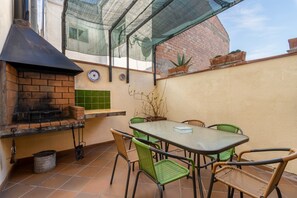 Een terras met een bakoven, groene stoelen, een tafel en een glazen constructie.