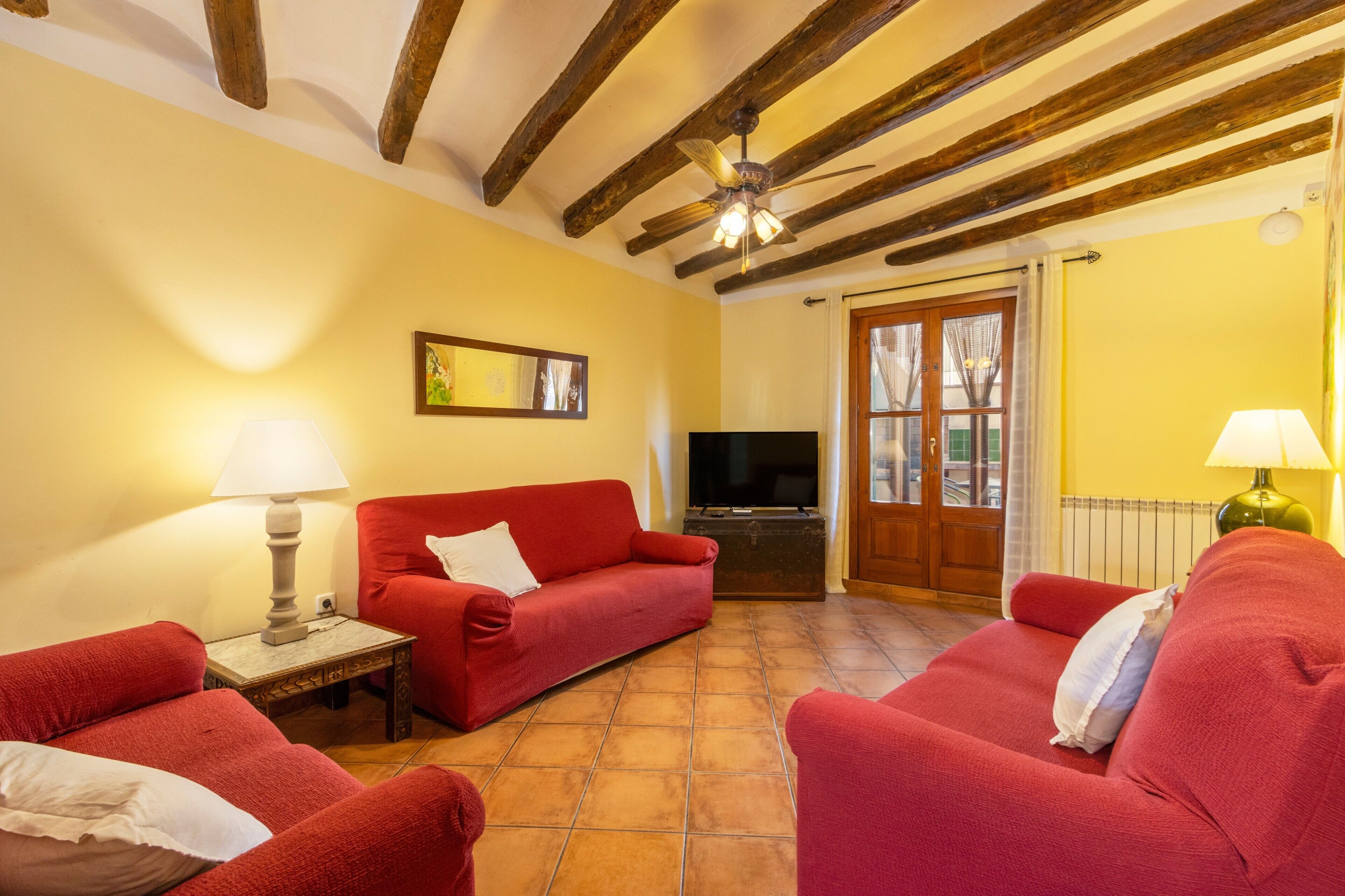 Uma sala de estar com um sofá vermelho, televisão, teto de madeira e piso ladrilhado.