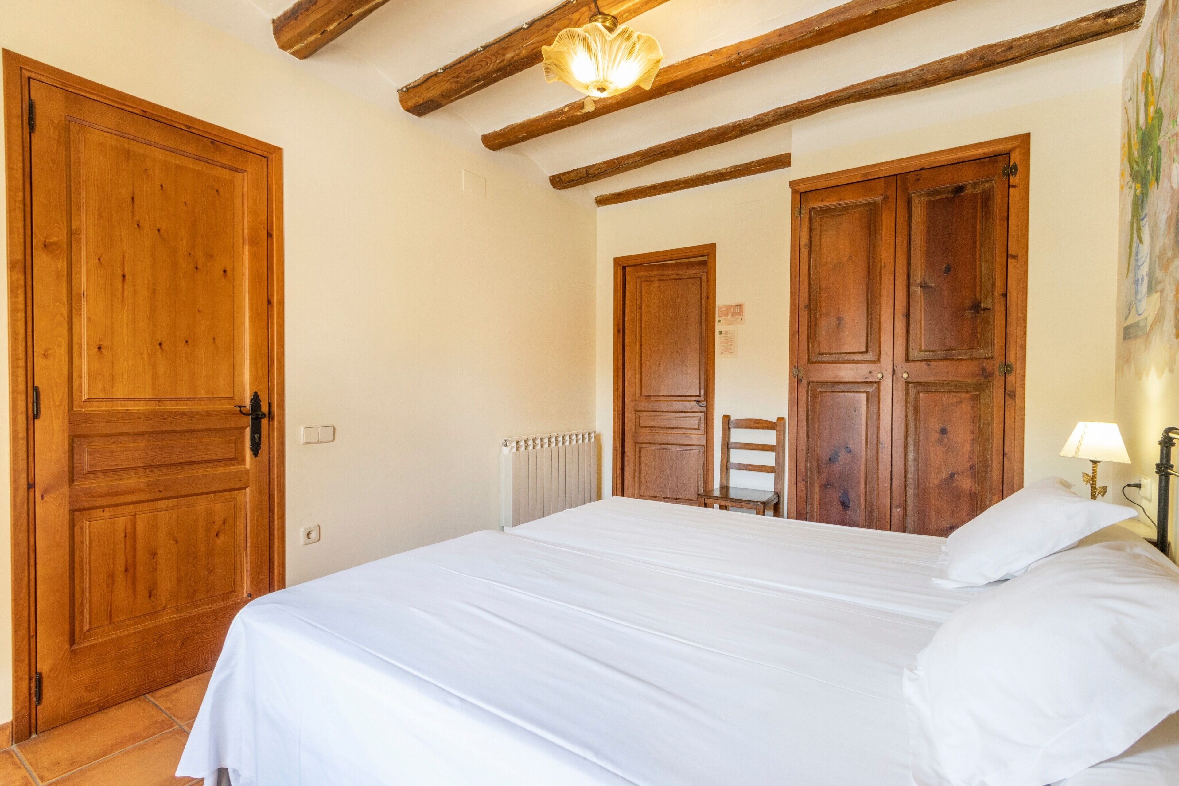 A bedroom with a bed, wooden doors, a radiator, and a chair.