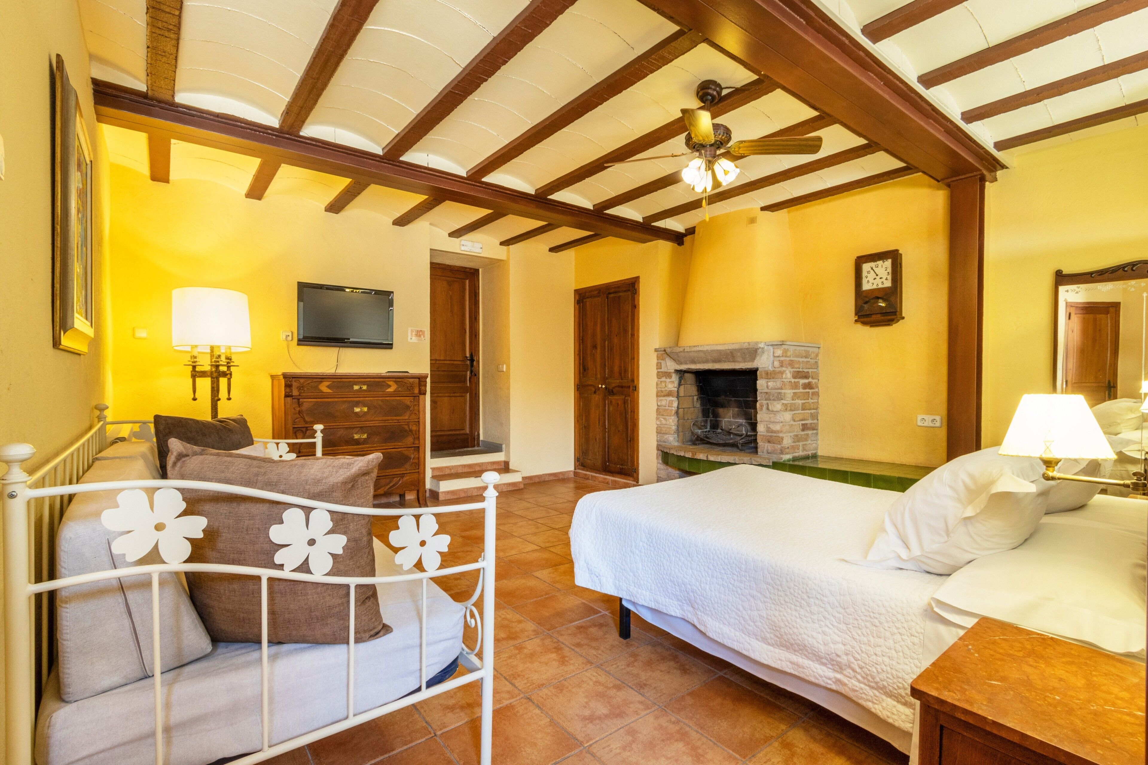 Una camera da letto con un letto, un comodino, una cassettiera, una televisione, un camino e travi in legno al soffitto.