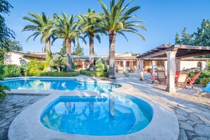 A swimming pool with a sunken center, surrounded by palm trees and a covered patio area. - Villa 'Can Vila' with Private Pool, Wi-Fi, and Air Conditioning (Illes Balears)