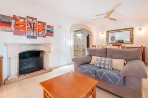 A living room with a fireplace, a sofa, a coffee table, and a ceiling fan. - Villa 'Can Vila' with Private Pool, Wi-Fi, and Air Conditioning (Illes Balears)