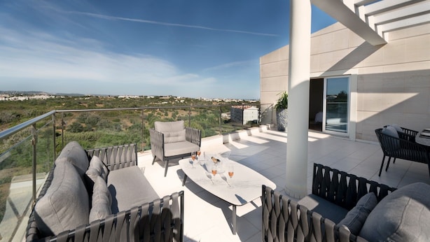 A terrace with outdoor furniture, a glass door leading to a room, and a view of the landscape.