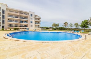A swimming pool with lounge chairs, a multi-story building with balconies, and a clear sky. - Apartment 'Monte Da Eira - Sunset' with Shared Pool, Wi-Fi and Air Conditioning (Albufeira)