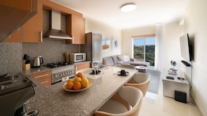 A modern kitchen with granite countertops, a dining area with a table and chairs, and a living room with a sofa and a TV.