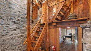 Una escalera de madera rústica con un muro de piedra, una mesa de madera y un extintor.