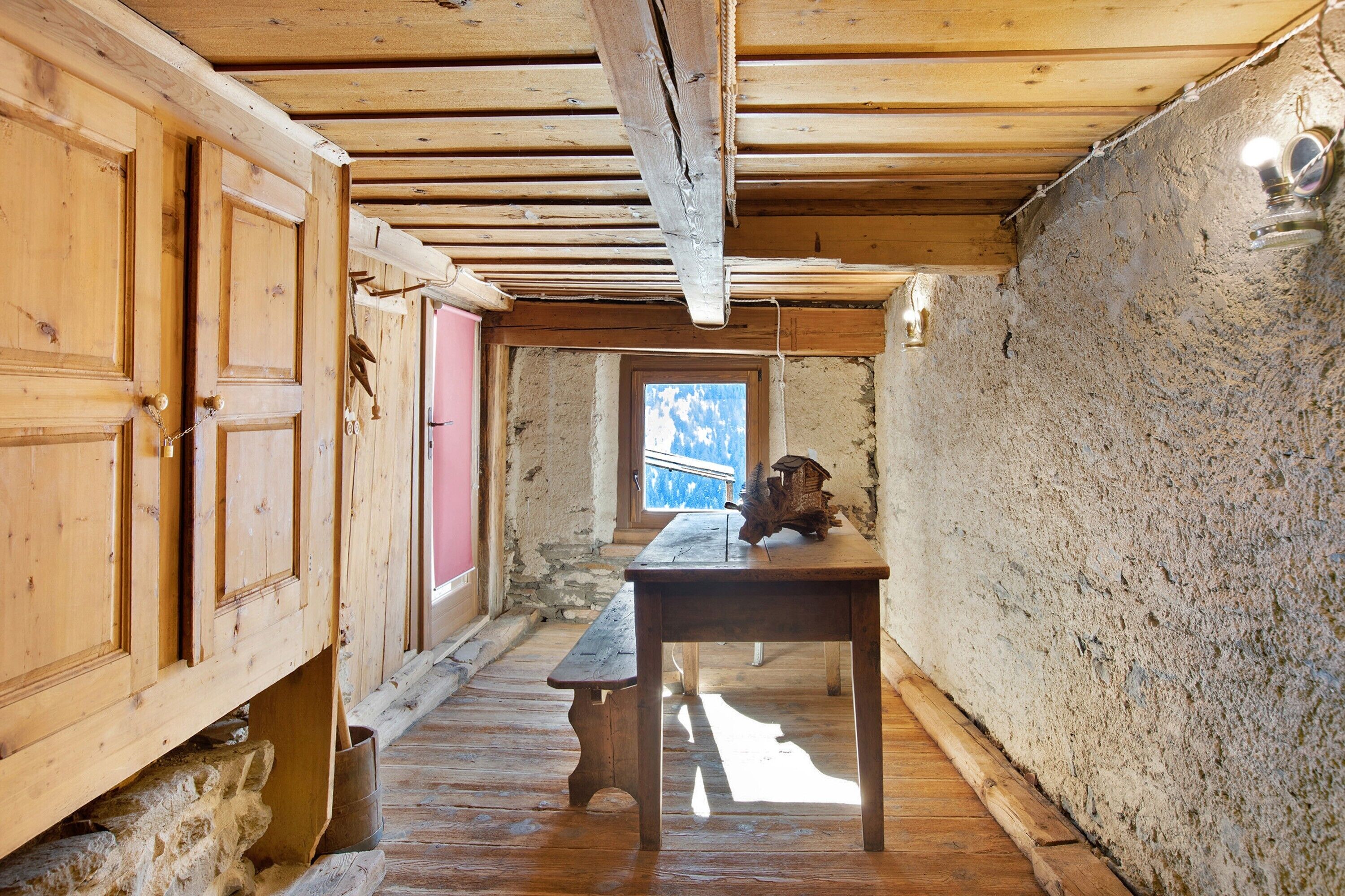 Ein rustikaler Holzraum mit Holztisch, einer Bank und einem Fenster mit Blick.
