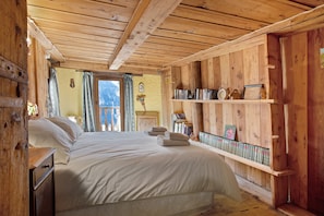 Una habitación de madera con una cama, estanterías llenas de libros y un ventanal con cortinas.