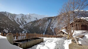Un paisaje montañoso nevado con una valla de madera, una estructura de piedra y un edificio de madera con tejados cubiertos de nieve.