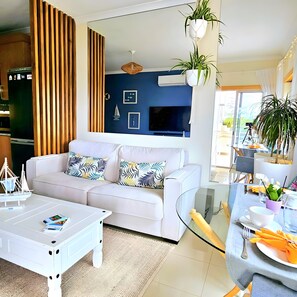 A modern living room with a white sofa, a glass coffee table, and a dining area with a glass table.