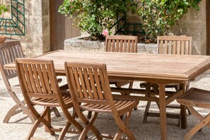 A wooden outdoor dining set with chairs and a table, surrounded by a stone wall and greenery.