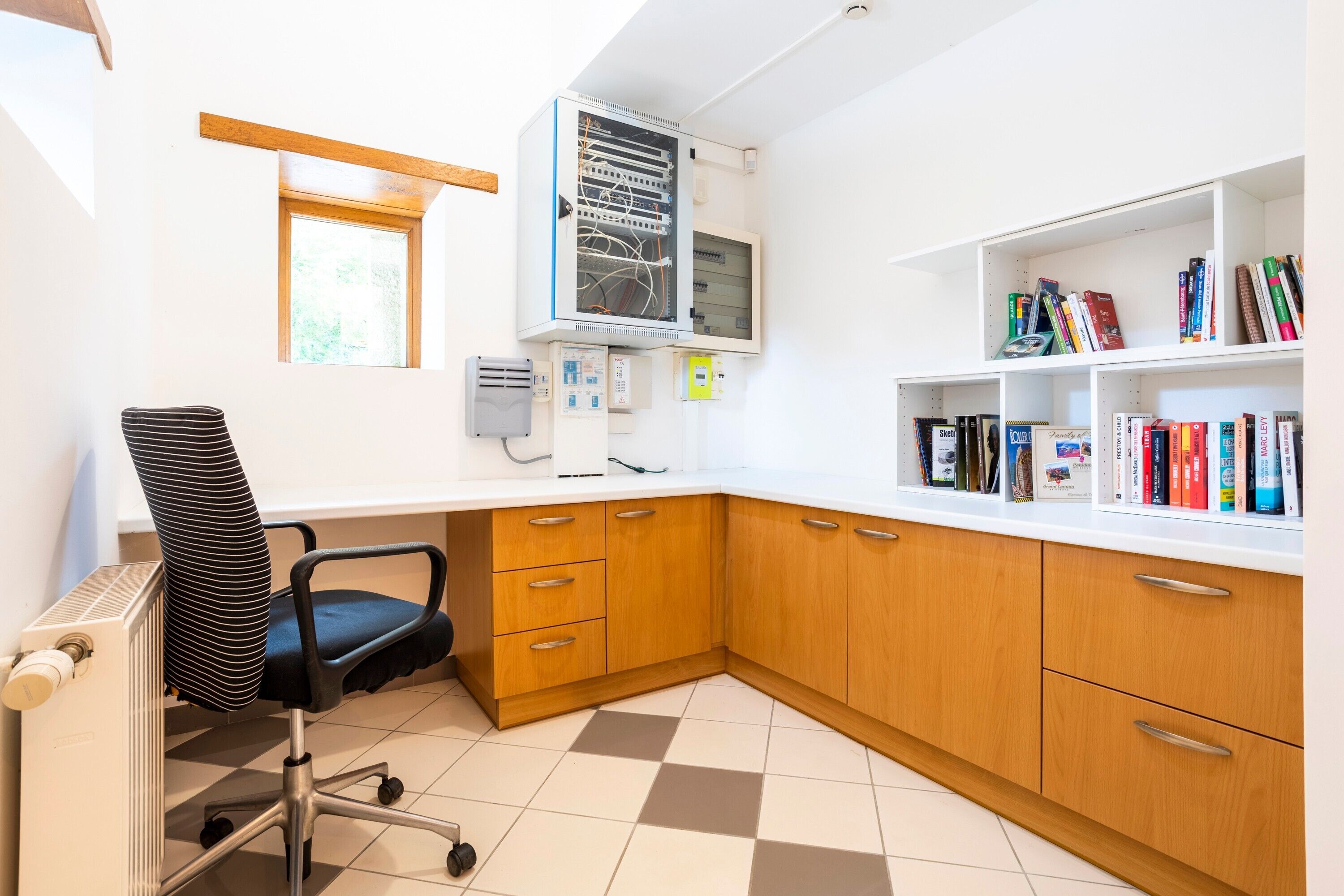 A corner office with a desk, chair, bookshelves, and a window.