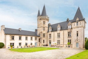 A large stone building with a central tower, multiple windows, and a paved courtyard.
