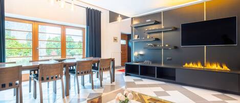 Una sala de estar moderna con comedor, chimenea y televisor grande.