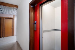 A hallway with a wooden door, a red elevator door, and a ceiling vent. - Apartment 'Le Morelle 2' with Balcony and Wi-Fi (Albenga)