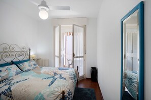 Ein Schlafzimmer mit Bett, Deckenventilator, Spiegel und einer Tür zu einem anderen Raum.