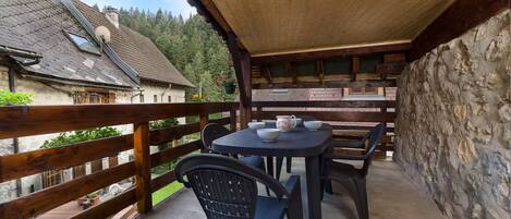 A covered outdoor area with a table and chairs, a stone wall, and a wooden fence.