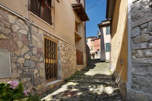 A narrow stone pathway between buildings with a metal gate and a small sign on the left.