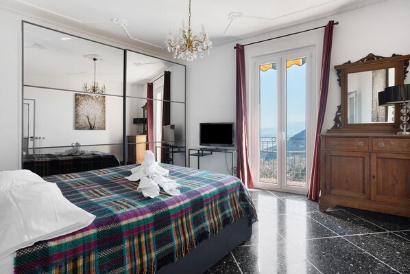 A bedroom with a bed, a TV, a dresser, a mirror, and a view of the outdoors.