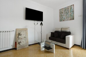 A modern living room with a flat-screen TV, a glass coffee table, a sofa, a radiator, and a painting on the wall.