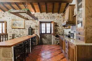A rustic kitchen with stone walls, wooden beams, and a tiled floor.
