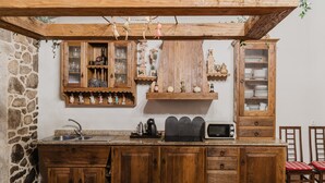 Maalaishenkinen keittiö, jossa on puiset kaapit, kiviseinä ja roikkuva kasvi.
