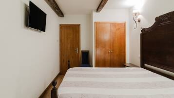 Un dormitorio con una cama, televisión montada en la pared, puertas de madera y una mesita de noche.