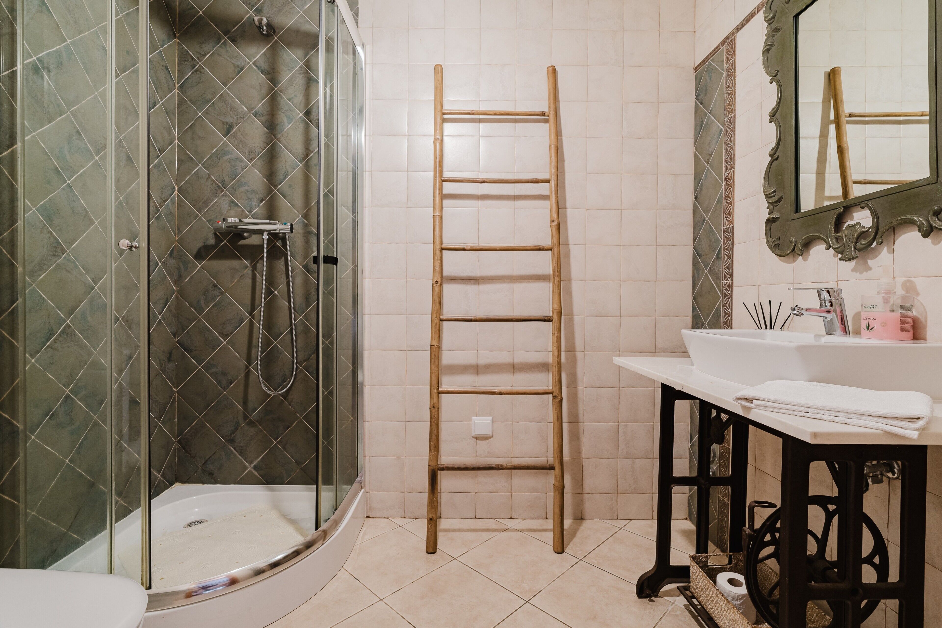 Un baño con cabina de ducha de vidrio, una escalera de madera, un lavabo con artículos de aseo y un espejo con marco decorativo.
