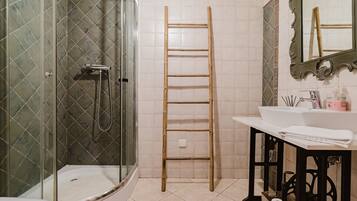 Un baño con cabina de ducha de vidrio, una escalera de madera, un lavabo con artículos de aseo y un espejo con marco decorativo.