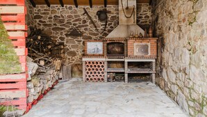 Cocina de paredes de piedra con horno de leña, un colgador para ollas y una pila de palets rojos y blancos.