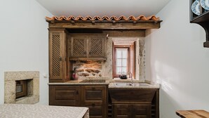 A compact kitchen with wooden cabinets, a stone wall, a window, and a tiled floor. - Room 'Familiar - 2' with Shared Terrace and Wi-Fi (Pitões das Junias)