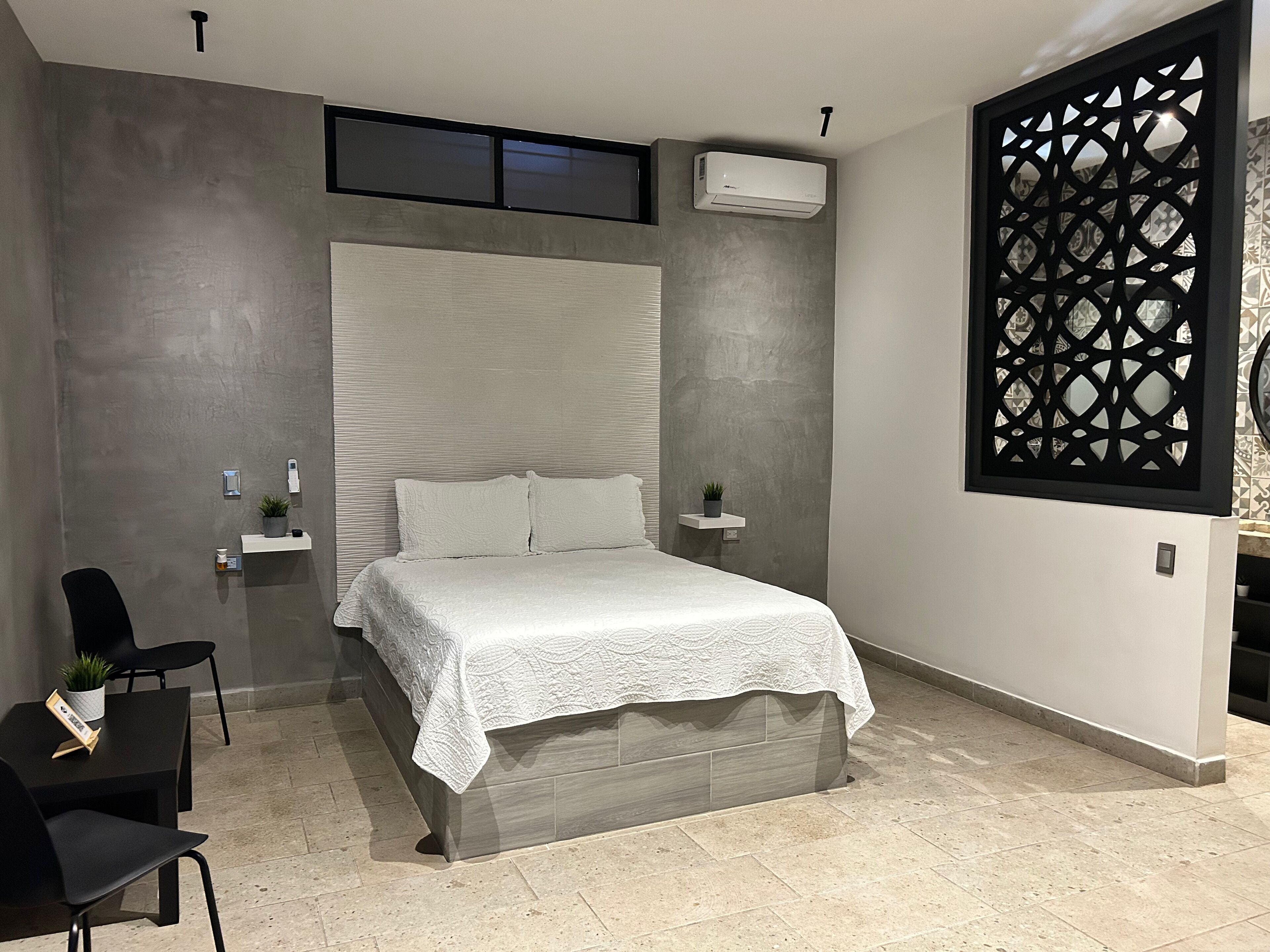 Une chambre à coucher moderne avec un grand lit, une petite table de chevet, une chaise et un élément de séparation décoratif.