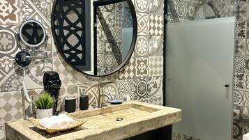 A bathroom with patterned tiles, a round mirror, a sink with a marble countertop, and a black shelf unit.