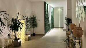 A modern interior with a hallway leading to a room, featuring potted plants, a geometric wall design, and a seating area with a table and chairs. - Wizard (Playas de Rosarito)