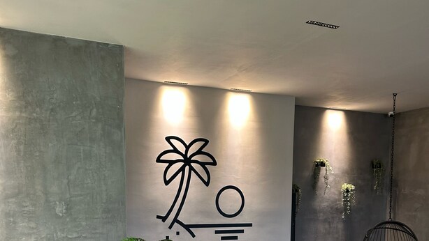 A modern indoor pool area with a large wall mural, a hanging chair, and various plants. - Wizard (Playas de Rosarito)