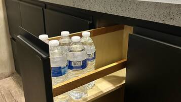 A kitchen with a countertop, a sink, and a drawer with water bottles.