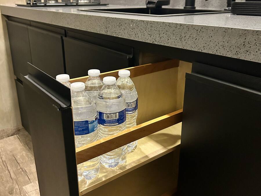 A kitchen with a countertop, a sink, and a drawer with water bottles.