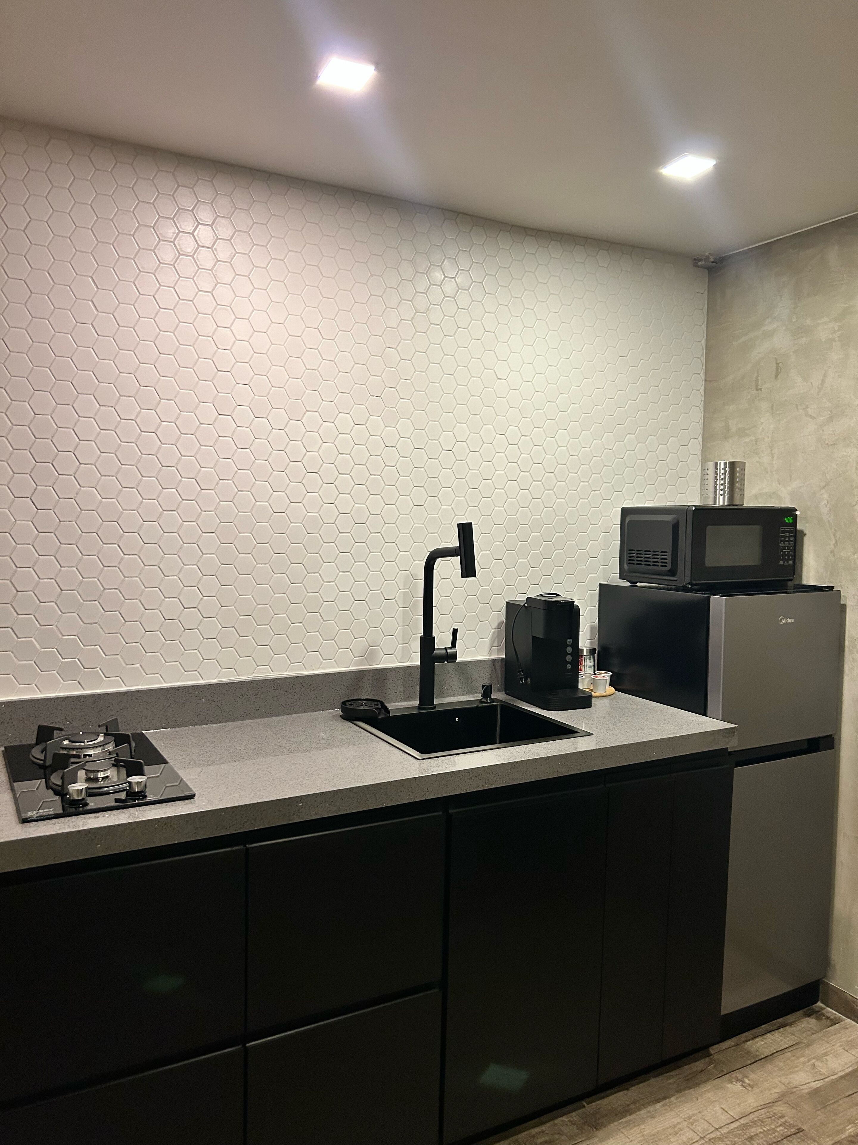Cocina moderna con un salpicadero de estilo hexagonal, un lavamanos negro, una estufa a gas, un microondas y una cafetera.