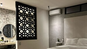 A modern bedroom with a bed, a decorative partition, a vanity with a mirror, and a wall-mounted air conditioner. - Wizard (Playas de Rosarito)