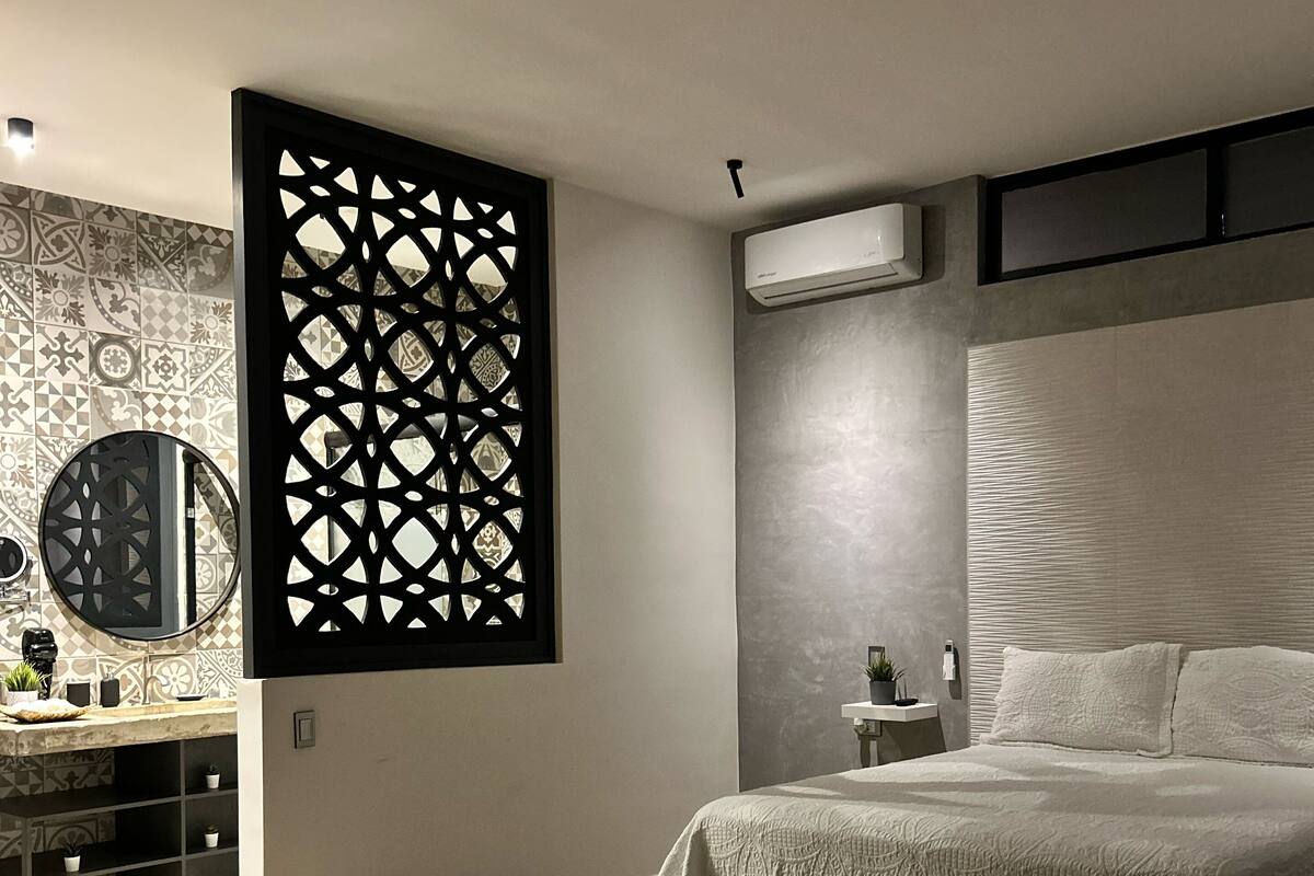 Quarto moderno com cama, divisória decorativa, toucador com espelho e ar condicionado fixado na parede.