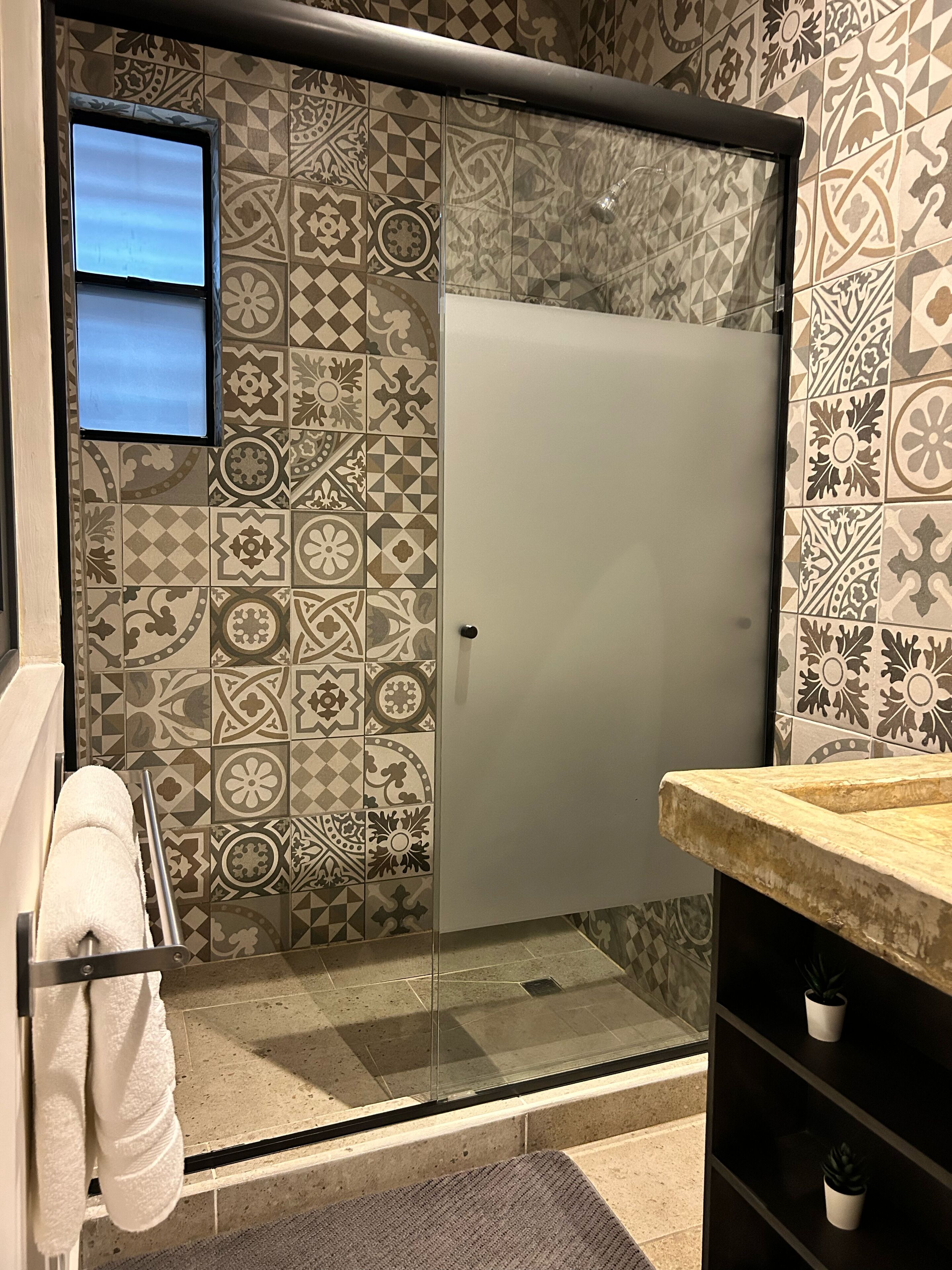 A bathroom with patterned tiles, a glass shower enclosure, a towel rack, and a sink with a countertop.