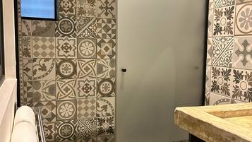A bathroom with patterned tiles, a glass shower enclosure, a towel rack, and a sink with a countertop.