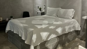 A modern bedroom with a large bed, a small bedside table, a potted plant, and a view of the sky through a window. - Wizard (Playas de Rosarito)