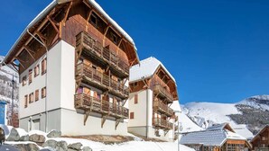 A chalet-style building with wooden balconies and a snow-covered roof, set against a mountainous backdrop. - Apartment in Saint-Sorlin with Mountain Views (Saint-Sorlin-d´Arves)