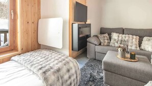 A cozy room with a bed, a sofa, a TV mounted on a wooden wall, and a fireplace. - Apartment in Saint-Sorlin with Mountain Views (Saint-Sorlin-d´Arves)