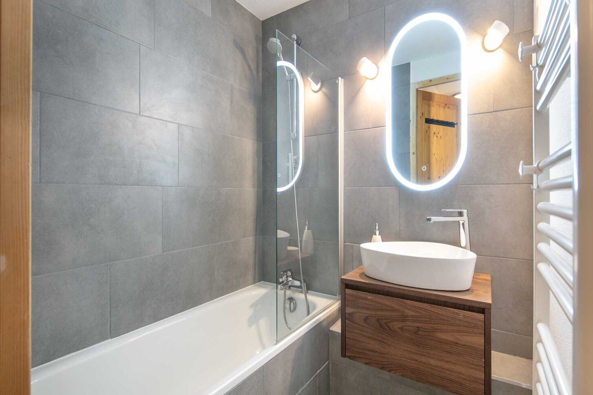 A modern bathroom with a bathtub, a wooden vanity, a large mirror with an oval frame, and a wall-mounted towel rack.